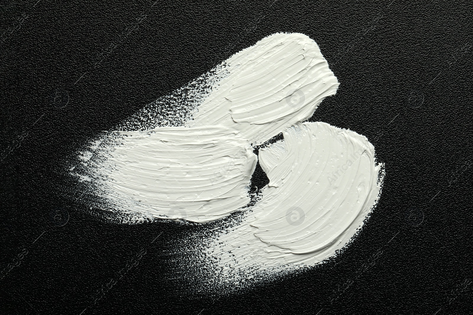 Photo of Strokes of white oil paint on black canvas, top view