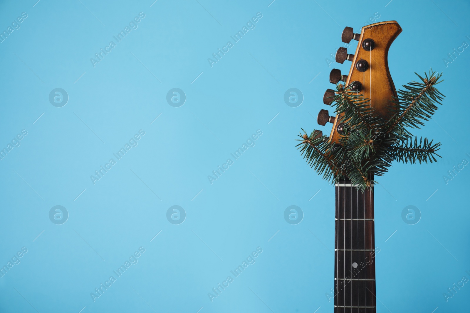 Photo of Guitar with fir tree branch on light blue background, space for text. Christmas music