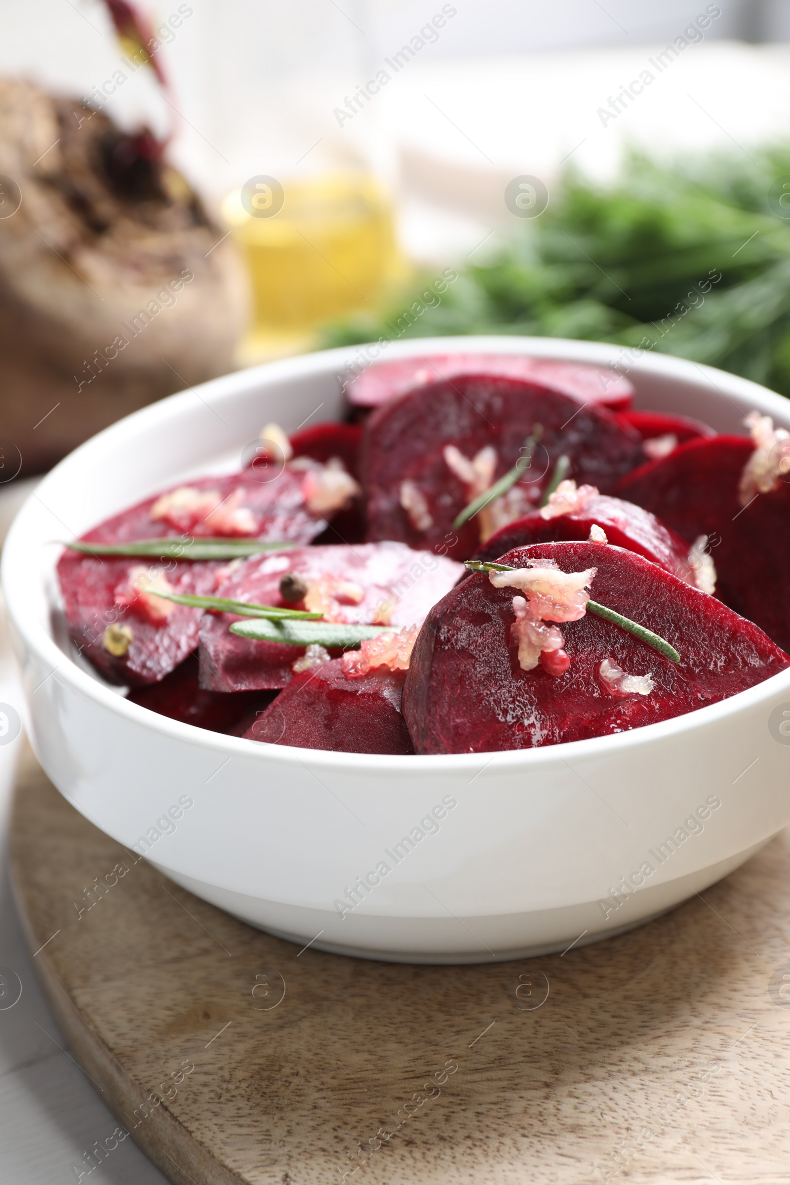 Photo of Bowl with raw beetroot slices, garlic and rosemary on wooden board, closeup