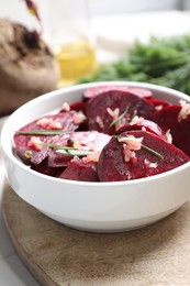 Photo of Bowl with raw beetroot slices, garlic and rosemary on wooden board, closeup