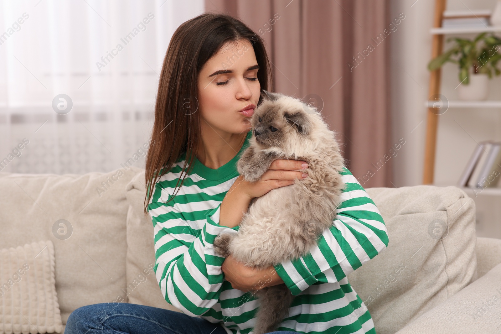 Photo of Woman kissing her cute cat on comfortable sofa at home