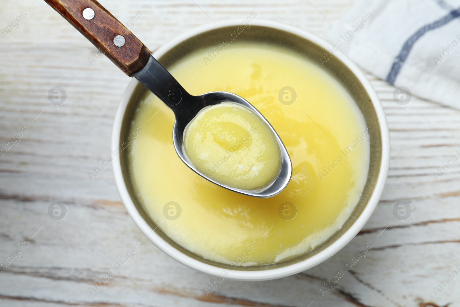 Photo of Bowl and spoon of Ghee butter on white wooden table, flat lay