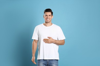 Photo of Happy healthy man touching his belly on light blue background