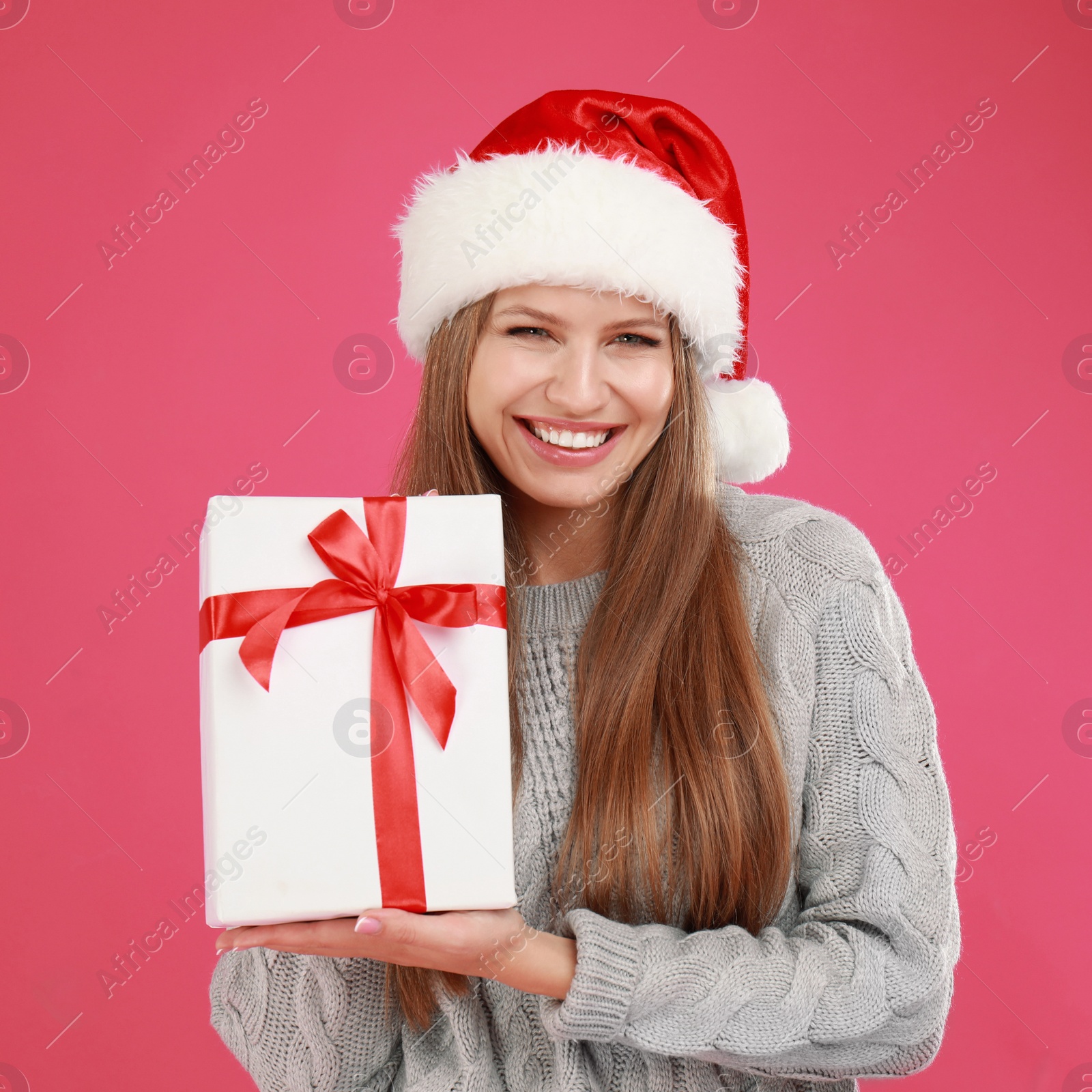 Photo of Happy young woman in Santa hat with Christmas gift on pink background