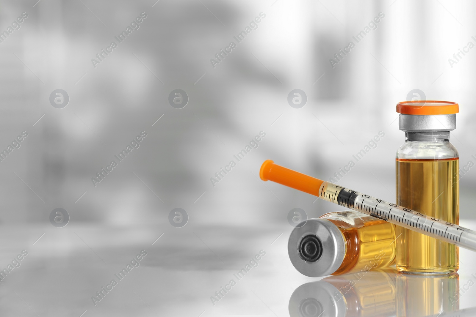 Photo of Glass vials and syringe with orange medication on white table, closeup. Space for text