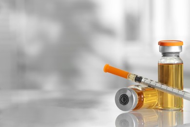 Photo of Glass vials and syringe with orange medication on white table, closeup. Space for text