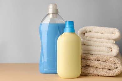 Photo of Bottles of fabric softener and stacked clean towels on pale yellow table against light grey background, space for text