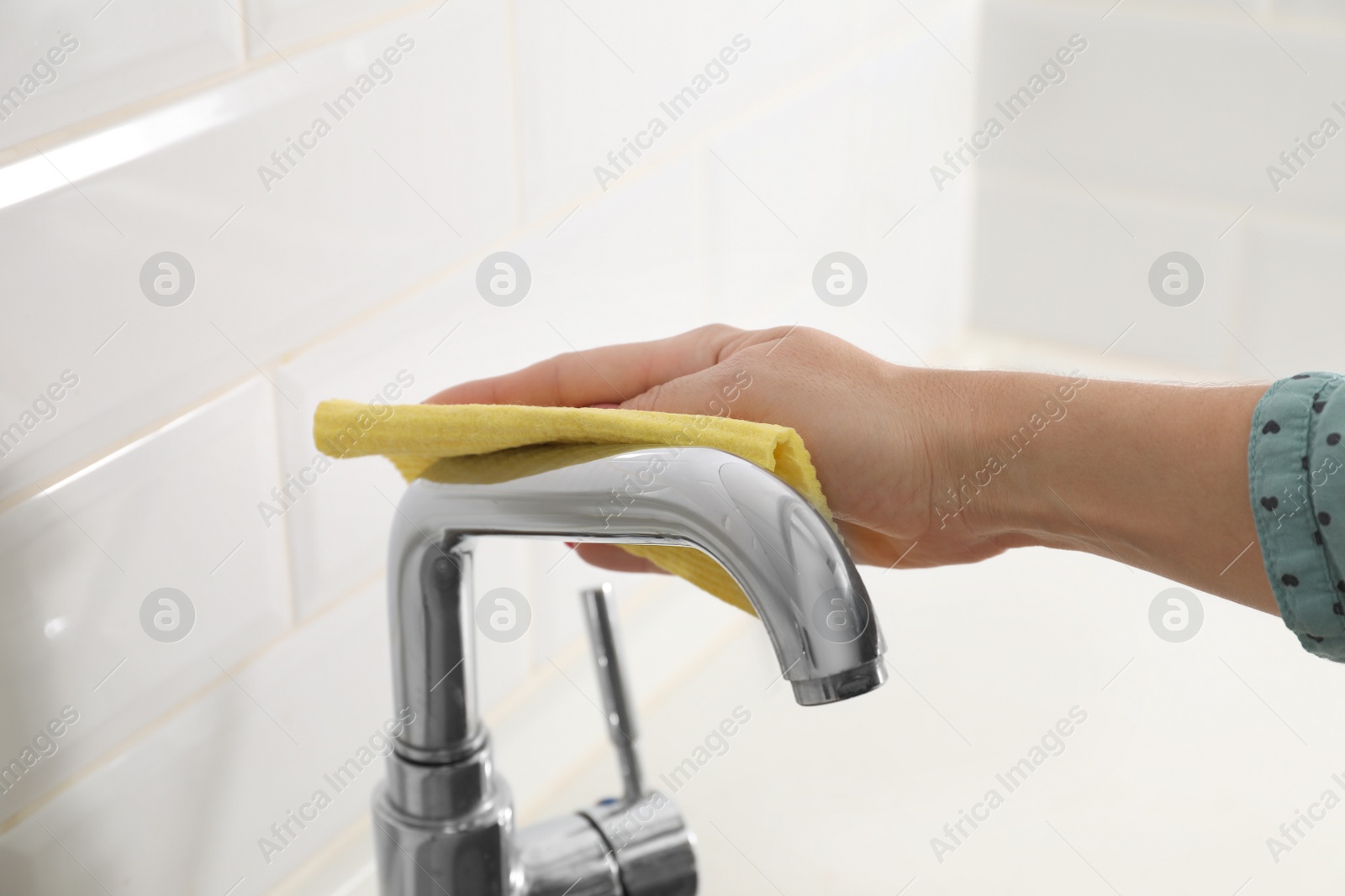 Photo of Woman cleaning tap with rag in kitchen, closeup