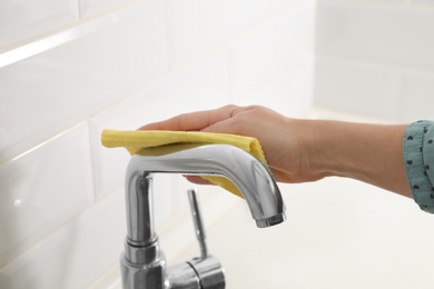 Woman cleaning tap with rag in kitchen, closeup