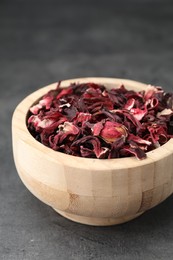 Photo of Hibiscus tea. Wooden bowl with dried roselle calyces on grey table, closeup