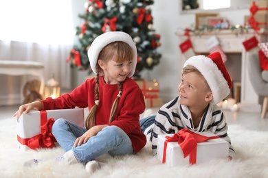 Photo of Cute little children in Santa hats with Christmas gift boxes at home
