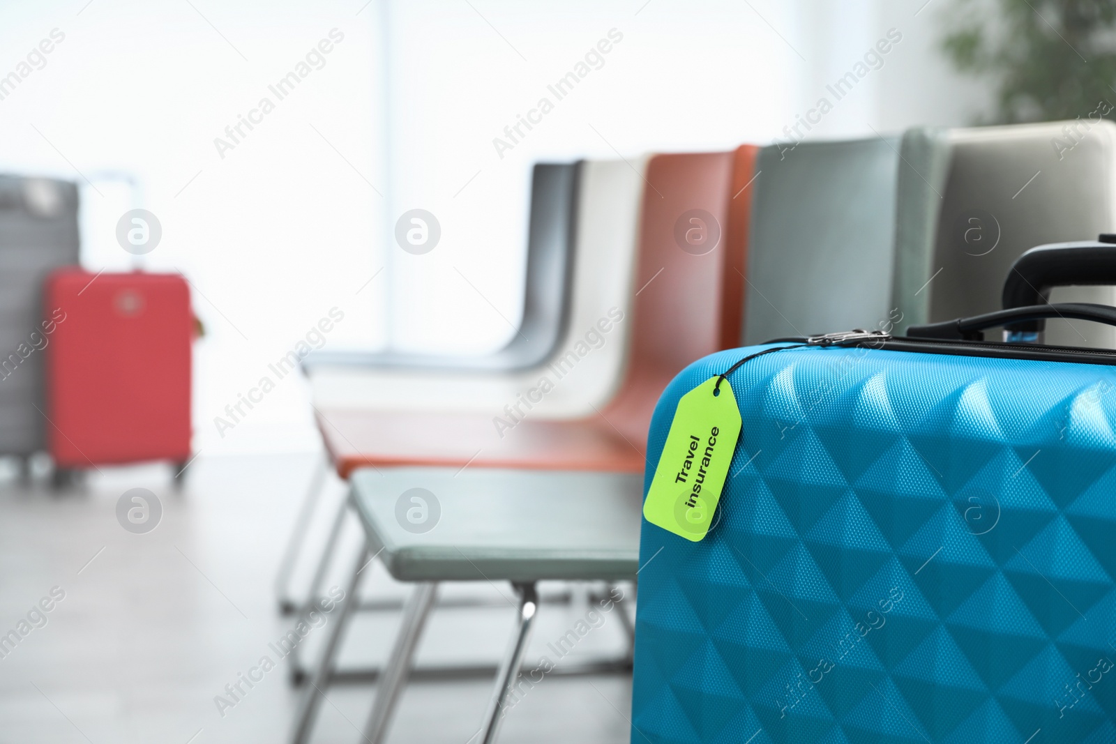 Photo of Blue suitcase with TRAVEL INSURANCE label indoors, closeup. Space for text