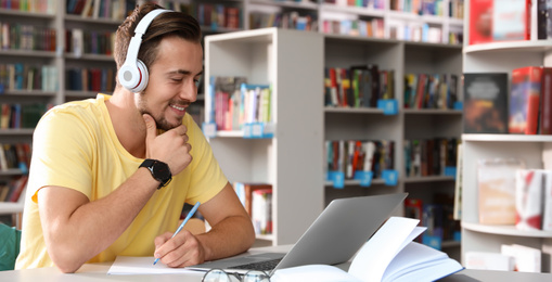 Image of Young student wearing headphones at table in modern library, space for text. Banner design