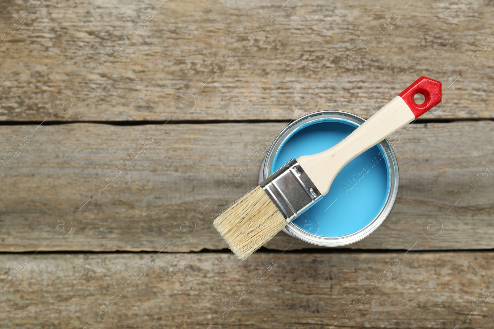 Photo of Can of light blue paint with brush on wooden table, top view. Space for text