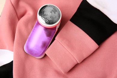 Photo of Modern fabric shaver on colorful sweater with lint, top view