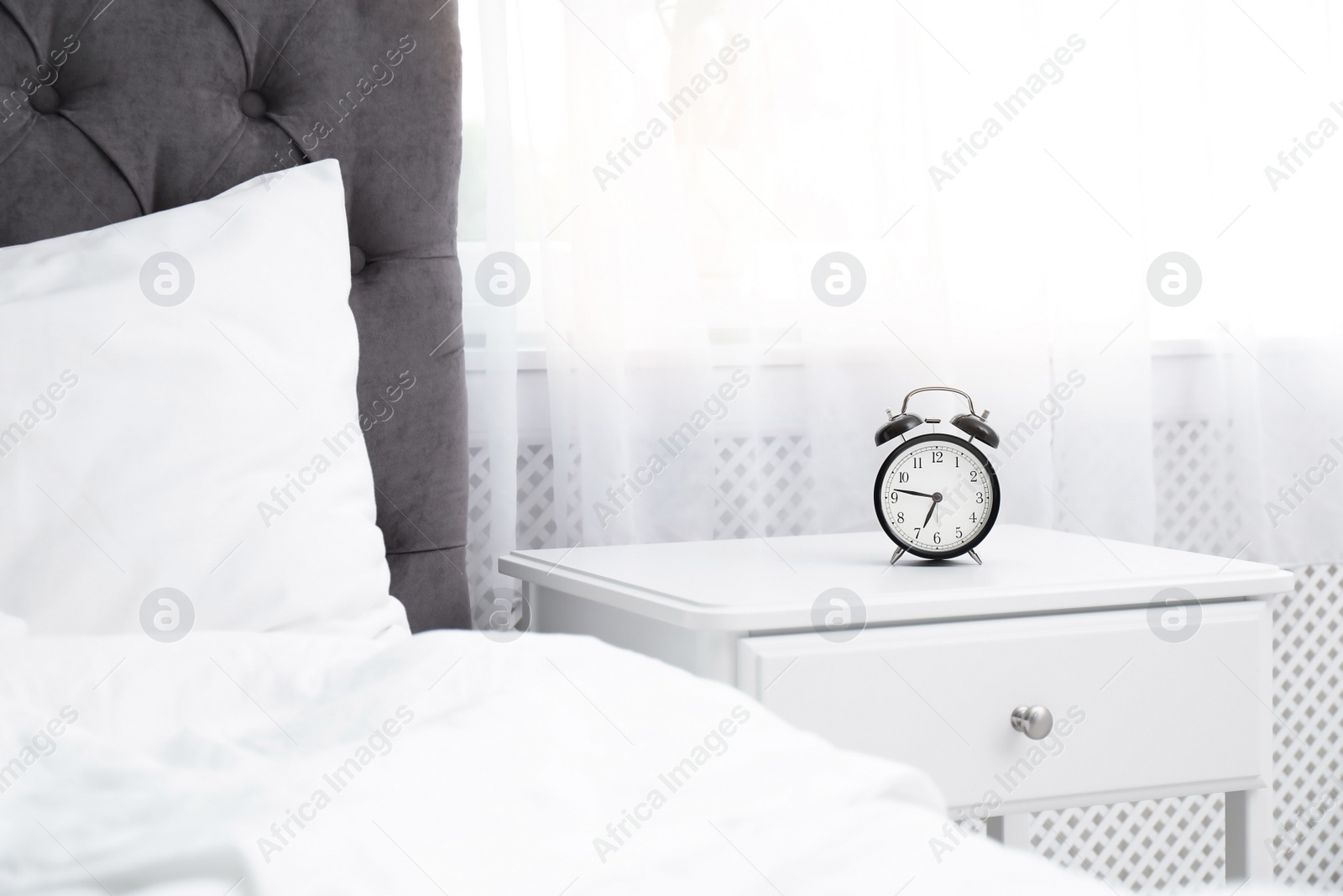 Photo of Analog alarm clock on table in bedroom. Time of day