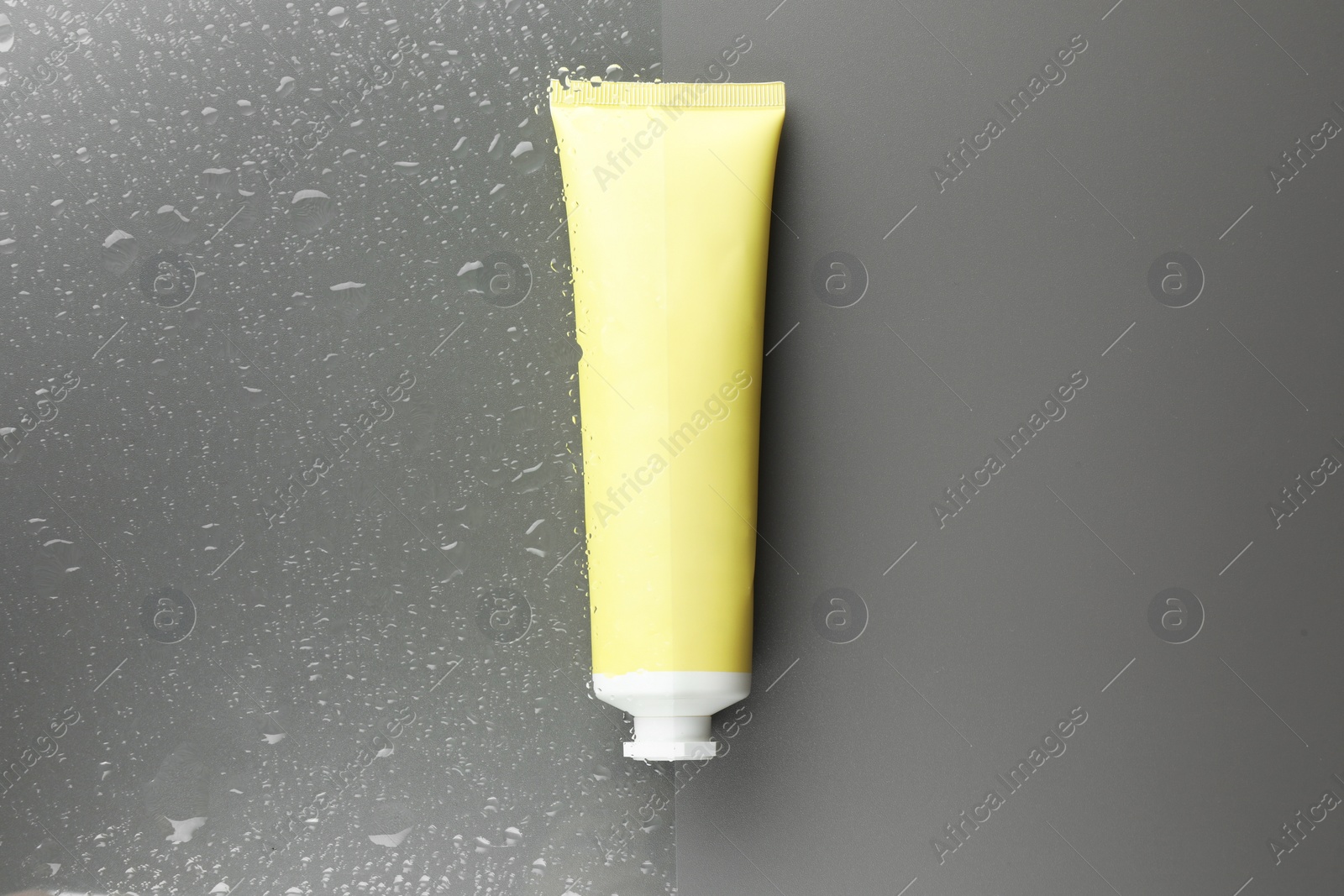 Photo of Tube with moisturizing cream on wet grey surface, top view