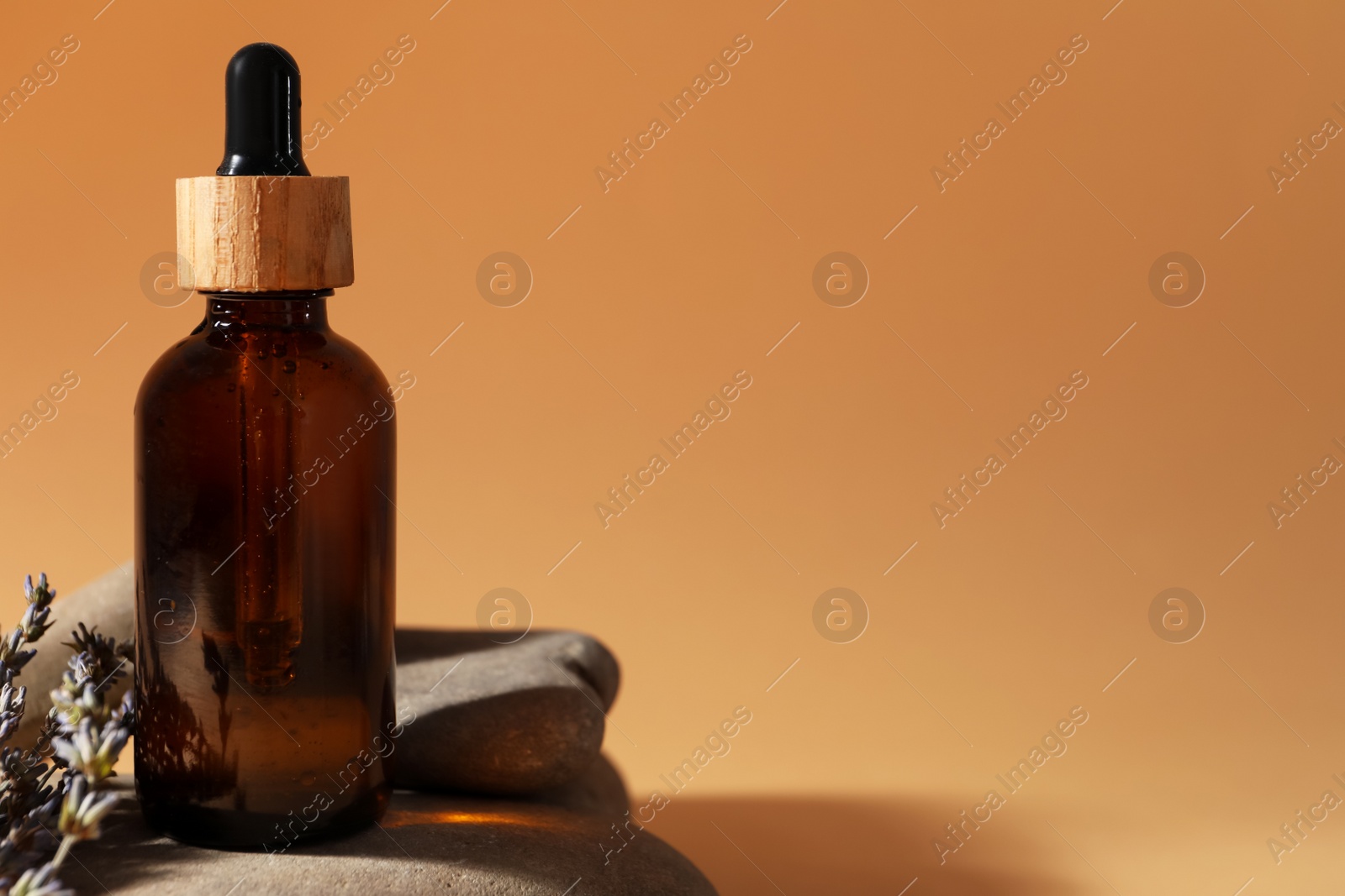 Photo of Bottle of face serum, spa stones and lavender flowers on beige background, closeup. Space for text