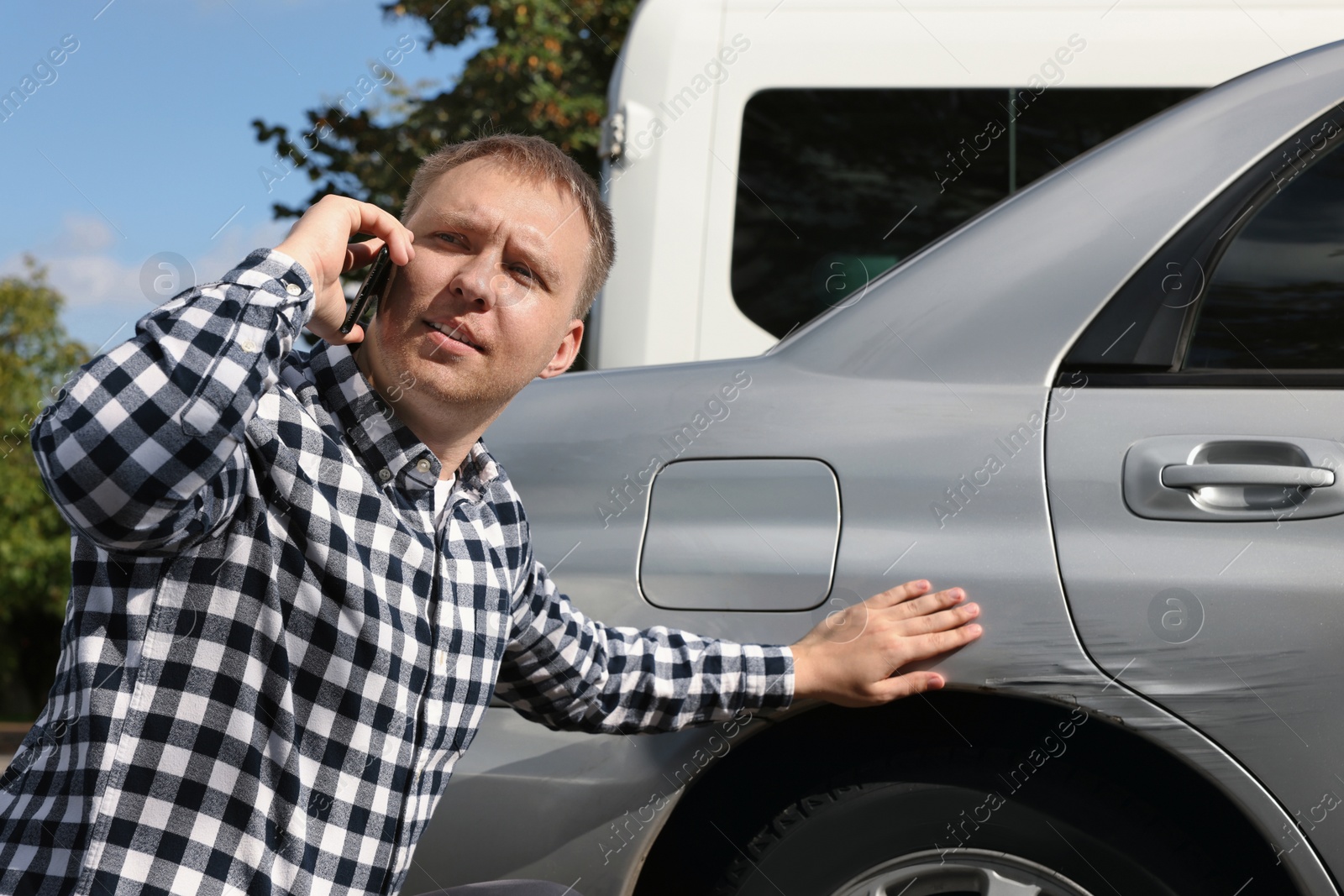 Photo of Man talking on phone near car with scratch outdoors