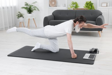 Photo of Senior man in sportswear exercising while watching online tutorial at home