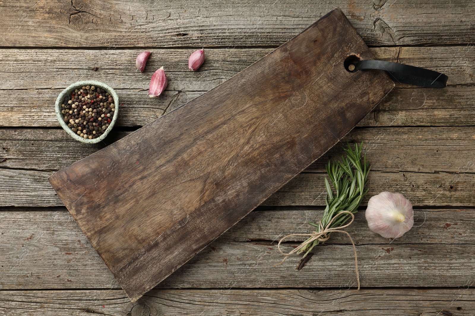 Photo of Cutting board, garlic, pepper and rosemary on wooden table, flat lay. Space for text