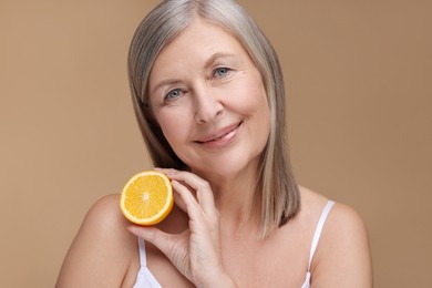 Beautiful woman with half of orange rich in vitamin C on beige background