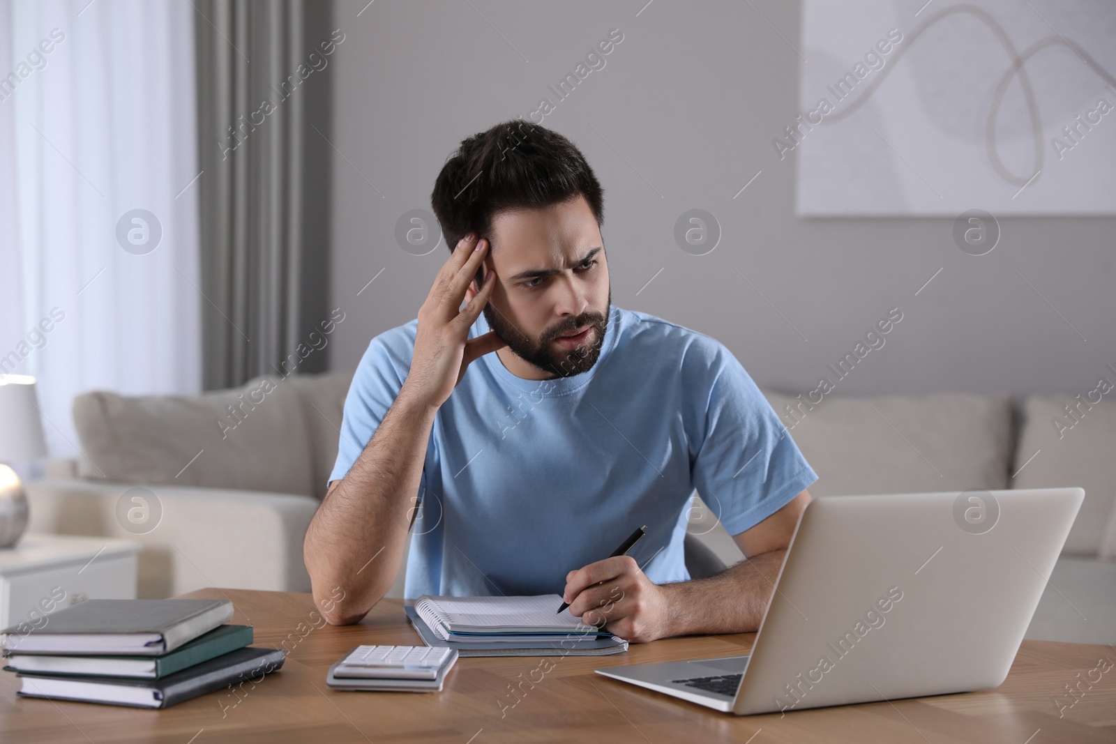 Photo of Confused young man watching webinar at table in room