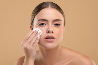 Photo of Beautiful woman removing makeup with cotton pad on beige background