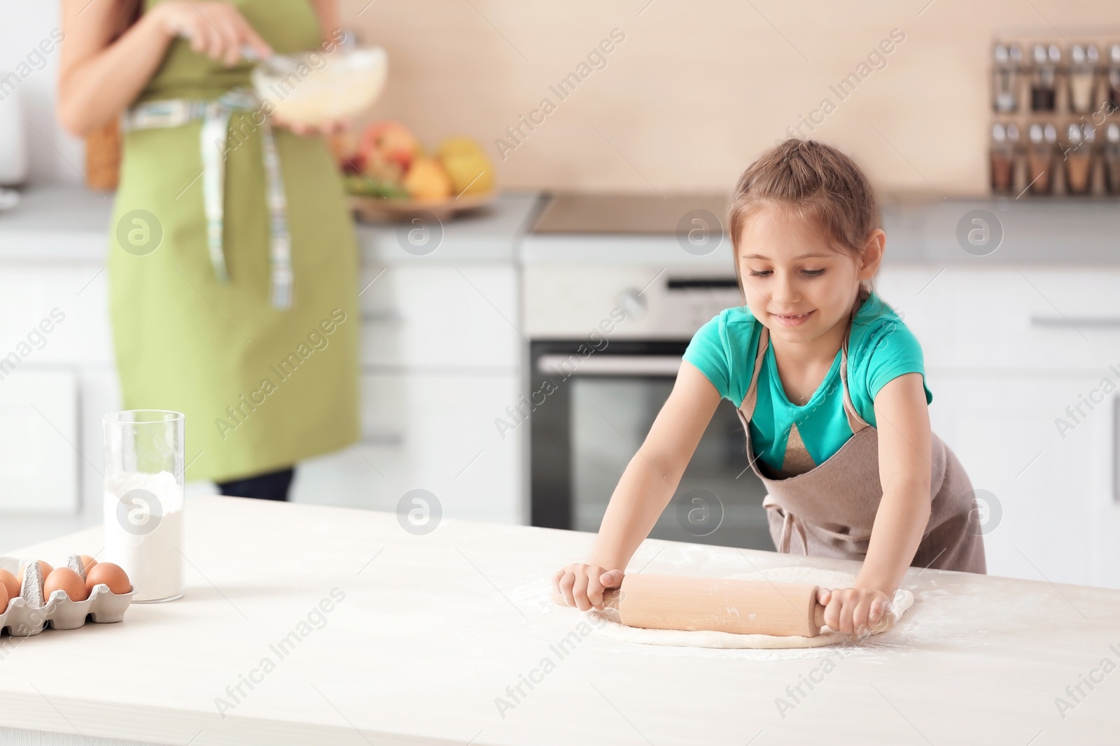 Photo of Mother and her daughter making dough at table in kitchen