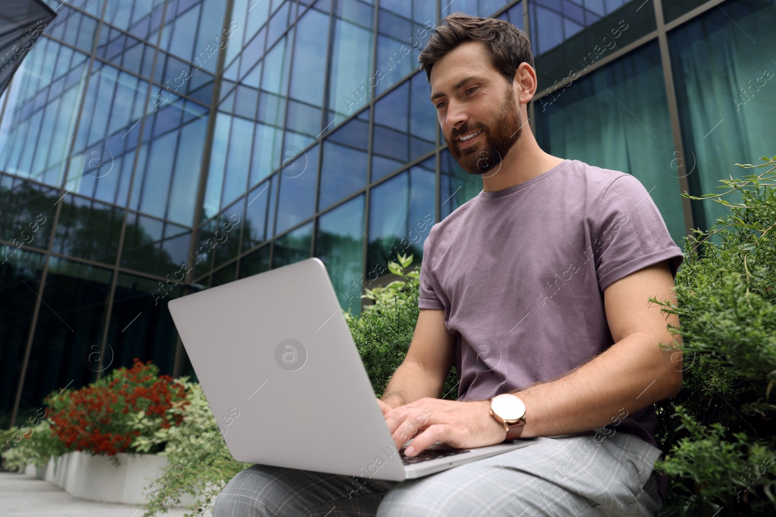 Photo of Handsome man with laptop near beautiful plants on city street