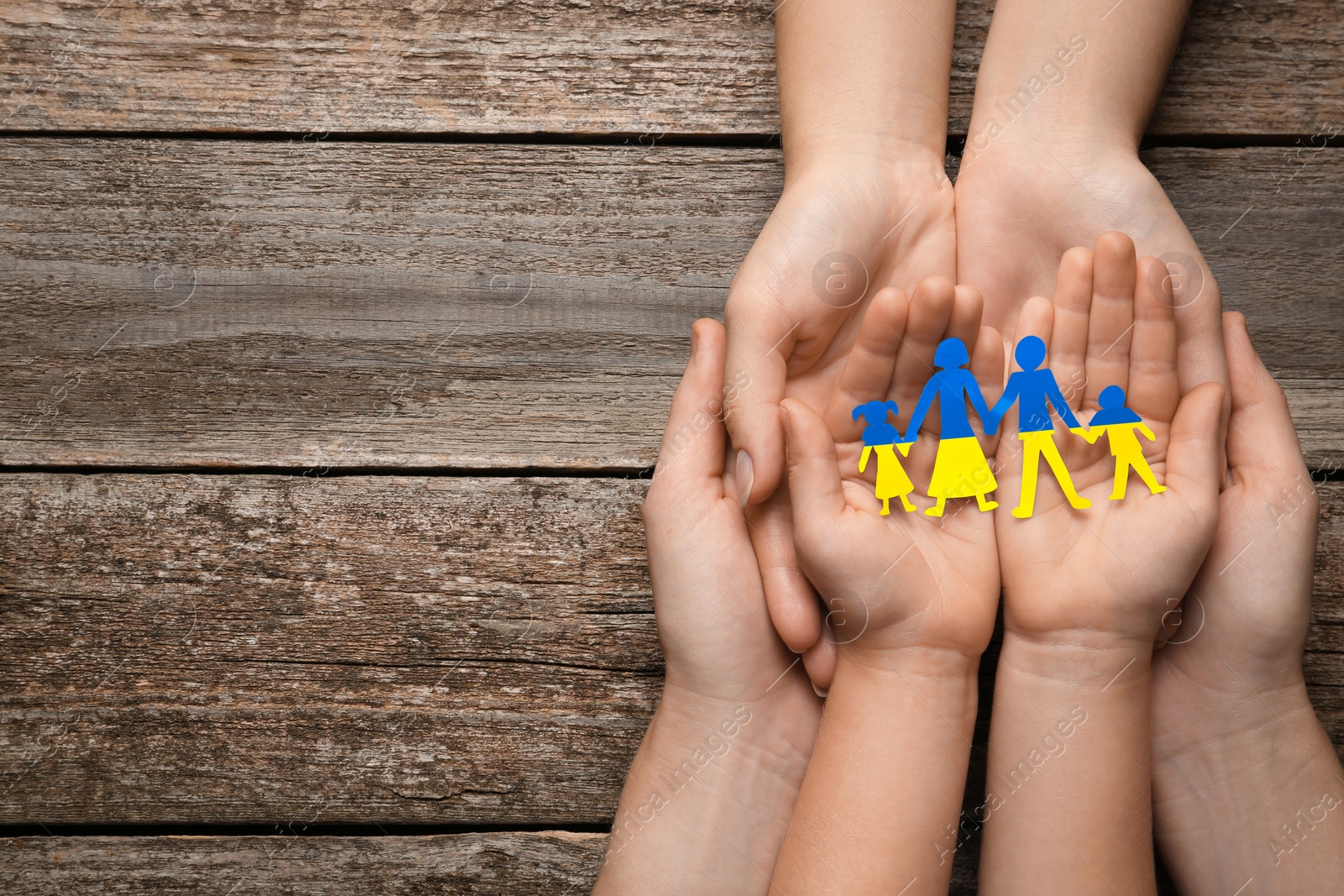 Image of Parents and child holding paper family cutout in colors of Ukrainian flag at wooden table, top view. Space for text