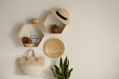 Photo of Hexagon wooden shelves with beautiful plants and accessories on light wall. Space for text