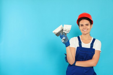 Professional worker in hard hat with putty knives on light blue background, space for text