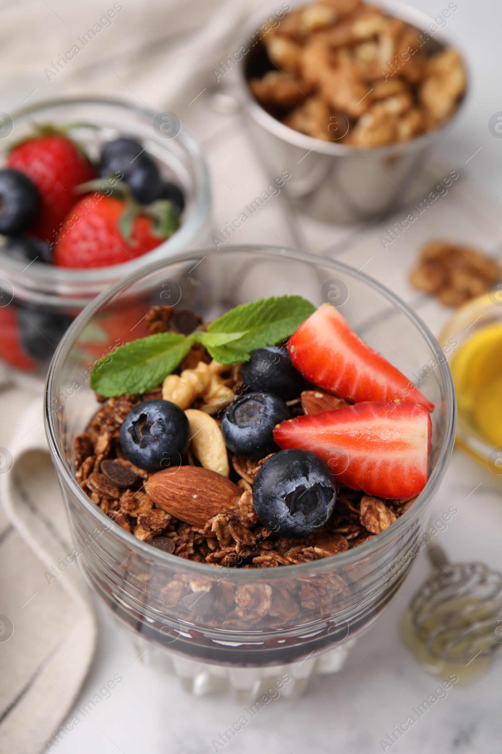 Photo of Tasty granola with berries and nuts in glass on white table, closeup