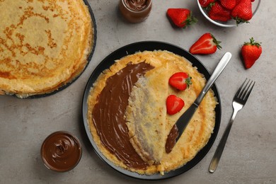 Photo of Delicious thin pancakes with chocolate spread and raspberries on grey table, flat lay