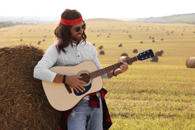 Photo of Hippie man playing guitar near hay bale in field