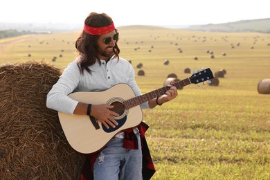 Hippie man playing guitar near hay bale in field