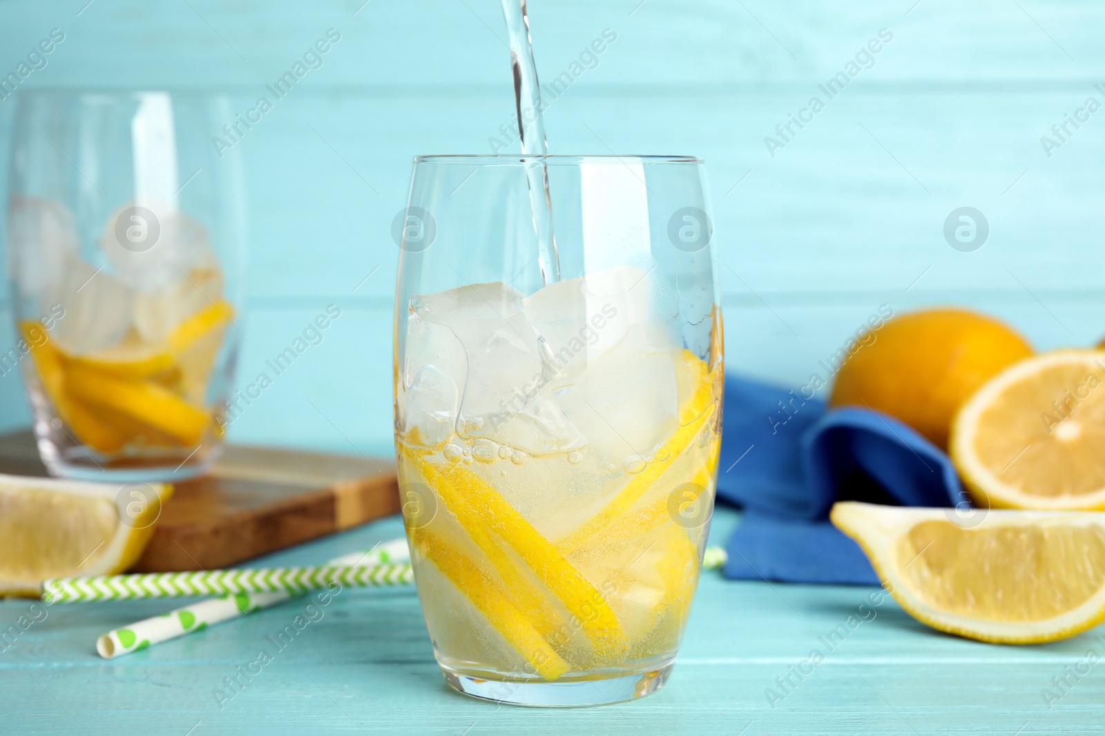 Photo of Pouring soda water into glass with lemon slices and ice cubes at light blue wooden table
