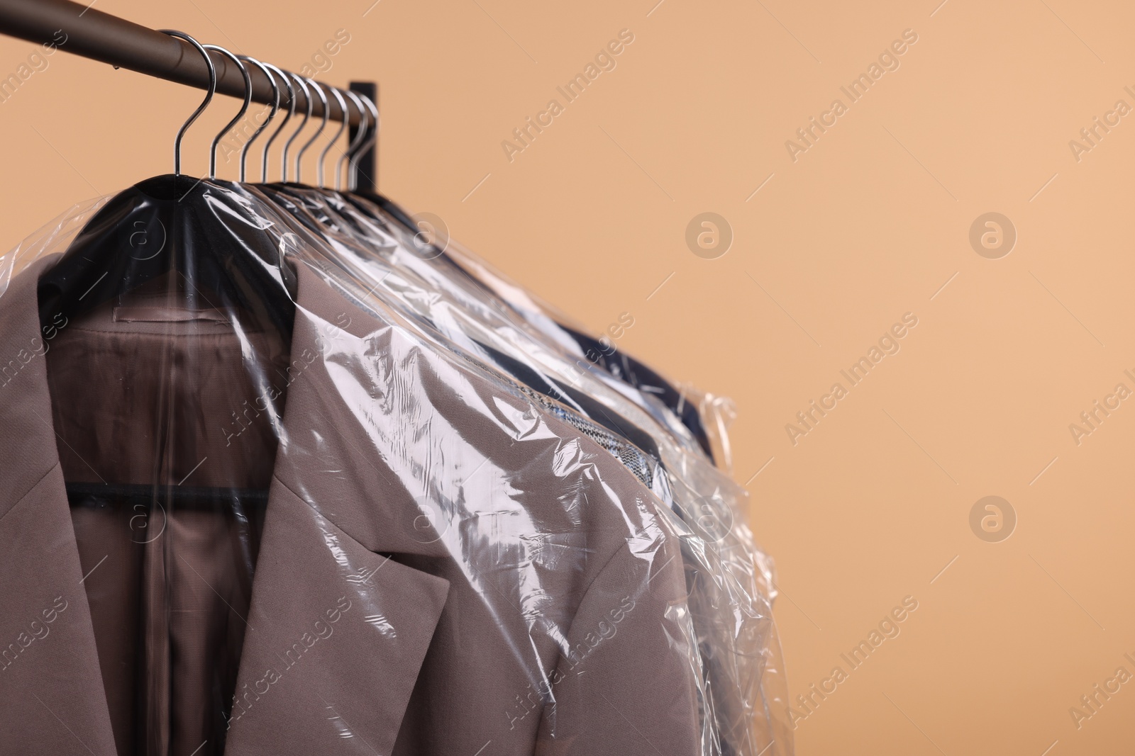 Photo of Dry-cleaning service. Many different clothes in plastic bags hanging on rack against beige background, space for text