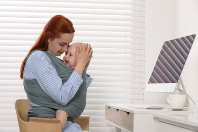 Photo of Mother holding her child in sling (baby carrier) at workplace