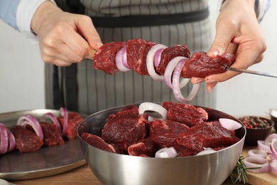 Woman stringing marinated meat on skewer at wooden table, closeup