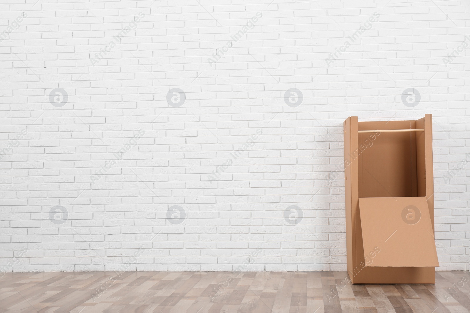 Photo of Empty cardboard wardrobe box against brick wall indoors. Space for text