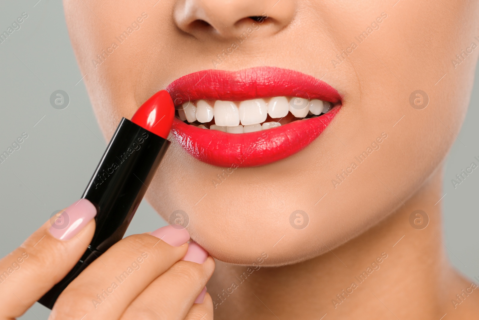 Photo of Young woman applying lipstick on color background, closeup