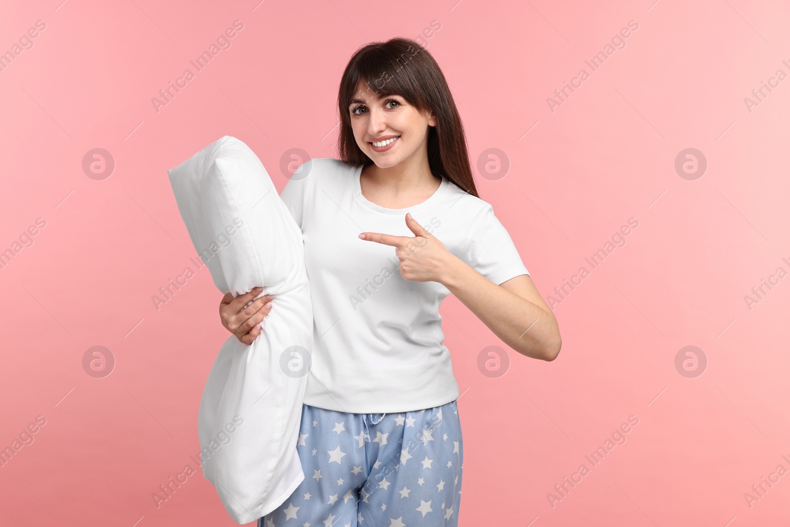 Photo of Happy woman in pyjama holding pillow on pink background