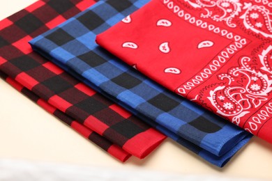 Folded bandanas with different patterns on beige background, closeup