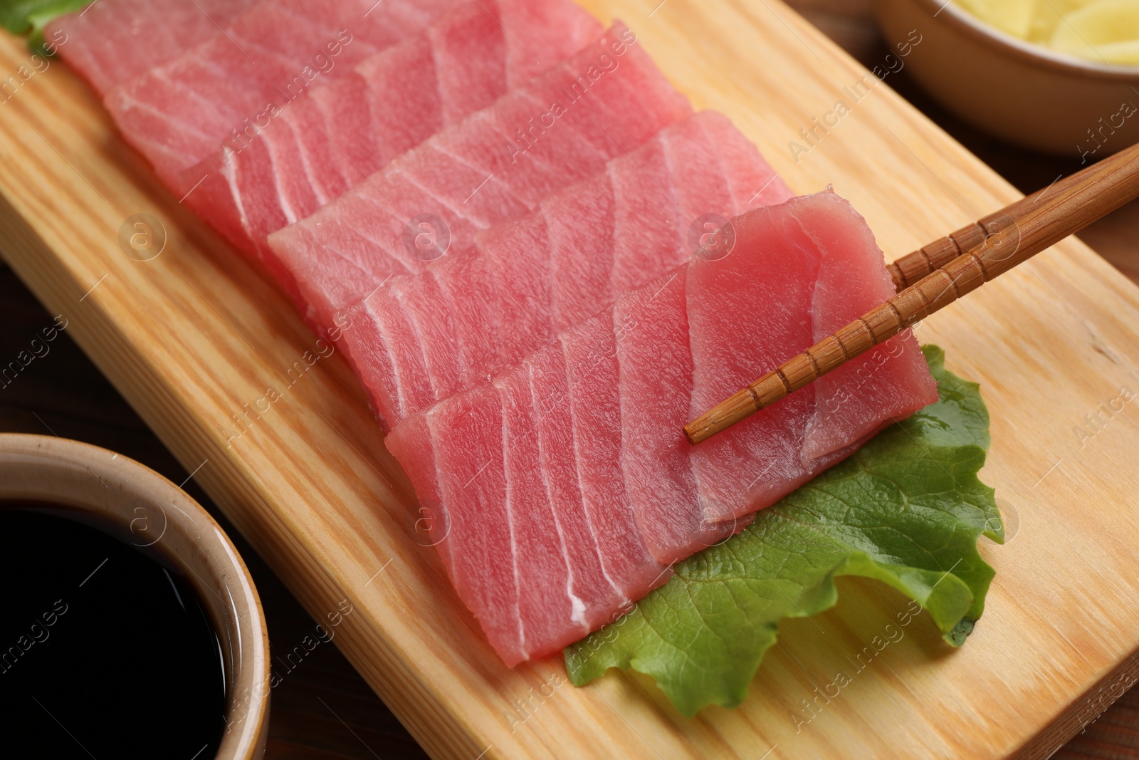 Photo of Taking tasty sashimi (piece of fresh raw tuna) from wooden board, closeup