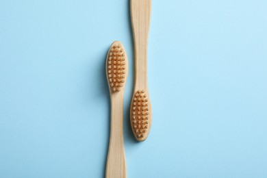 Two bamboo toothbrushes on light blue background, flat lay