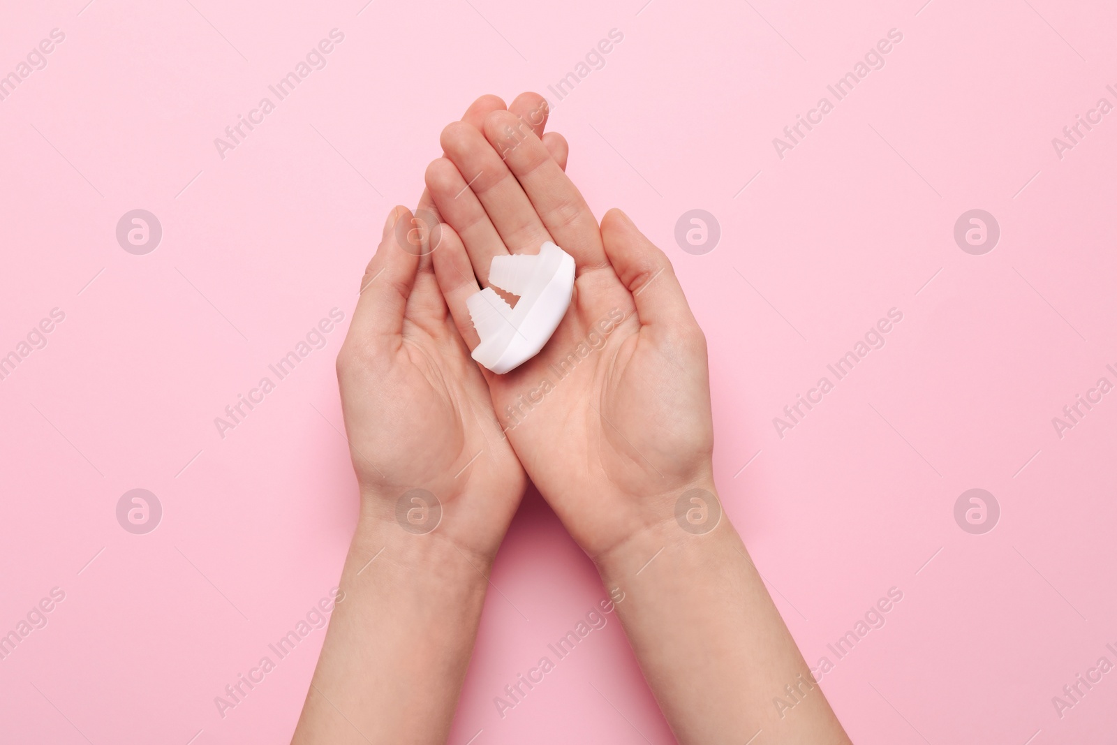 Photo of Woman holding anti-snoring device for nose on pink background, top view