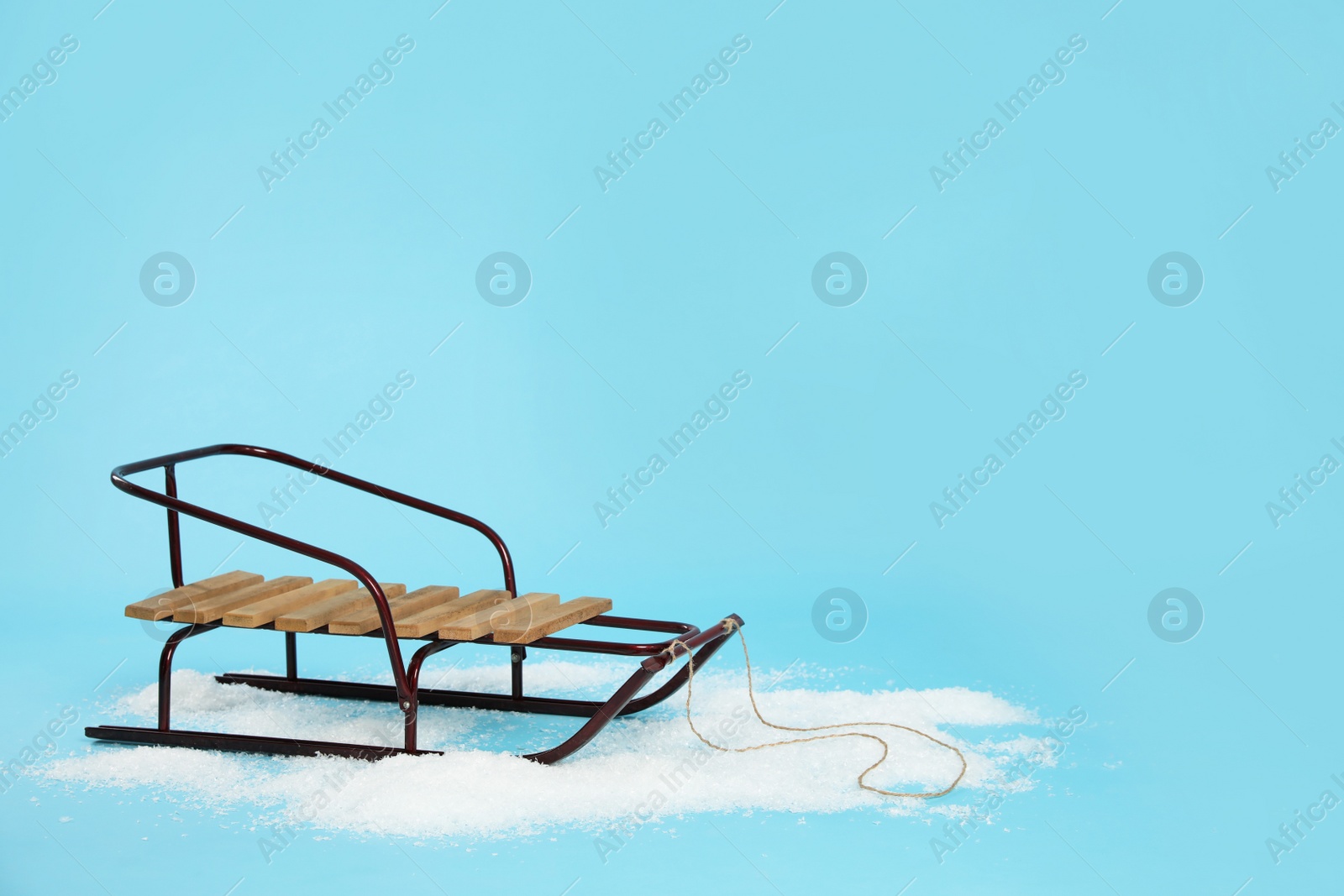 Photo of Stylish sleigh in pile of snow on light blue background, space for text