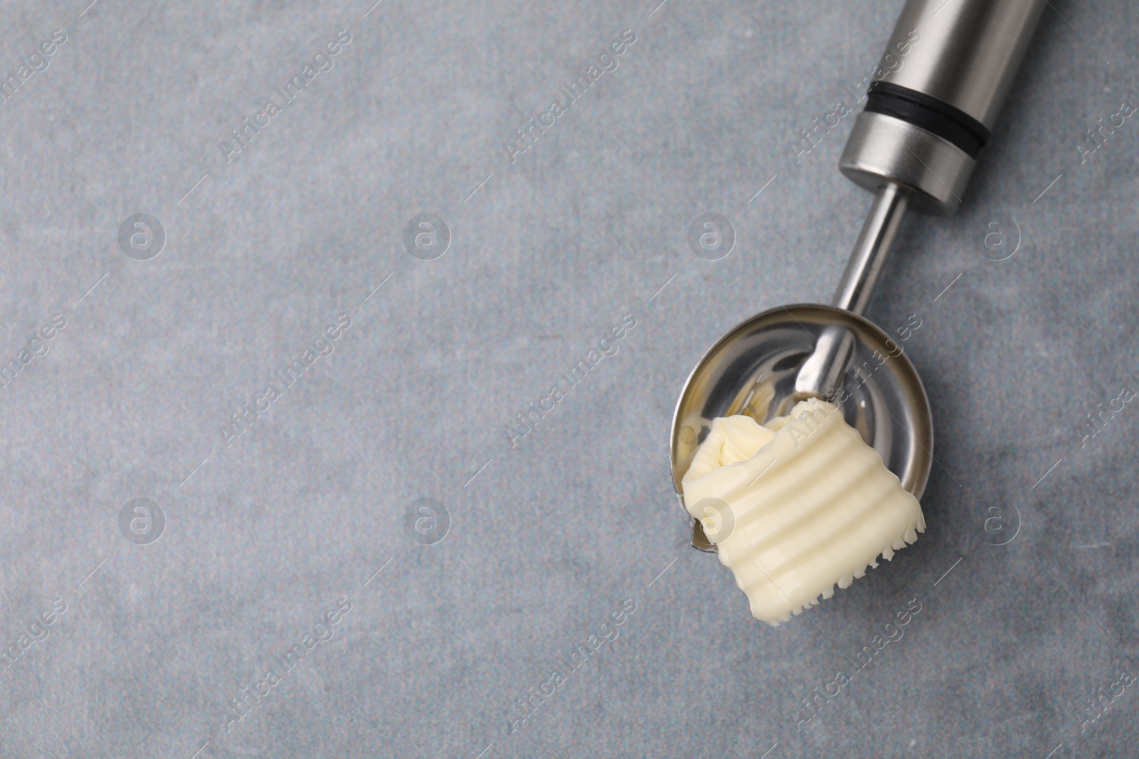 Photo of Tasty butter curl in spoon on light grey table, top view. Space for text